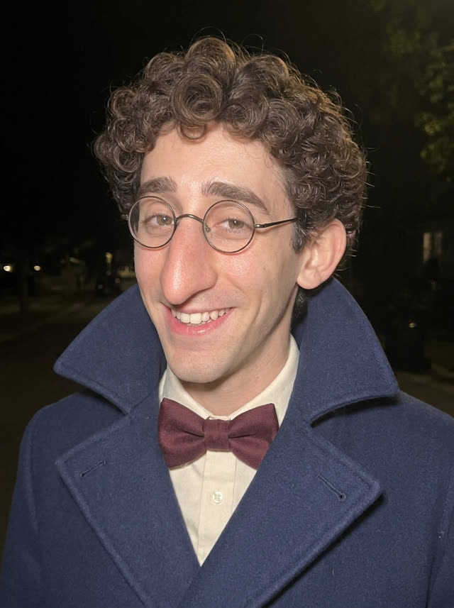 Percival Beaksley in a navy double-breasted coat and burgundy bow tie